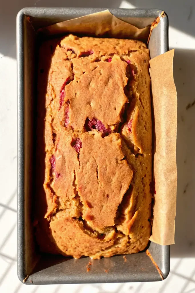 Freshly baked gluten free lemon raspberry loaf in a parchment-lined metal pan